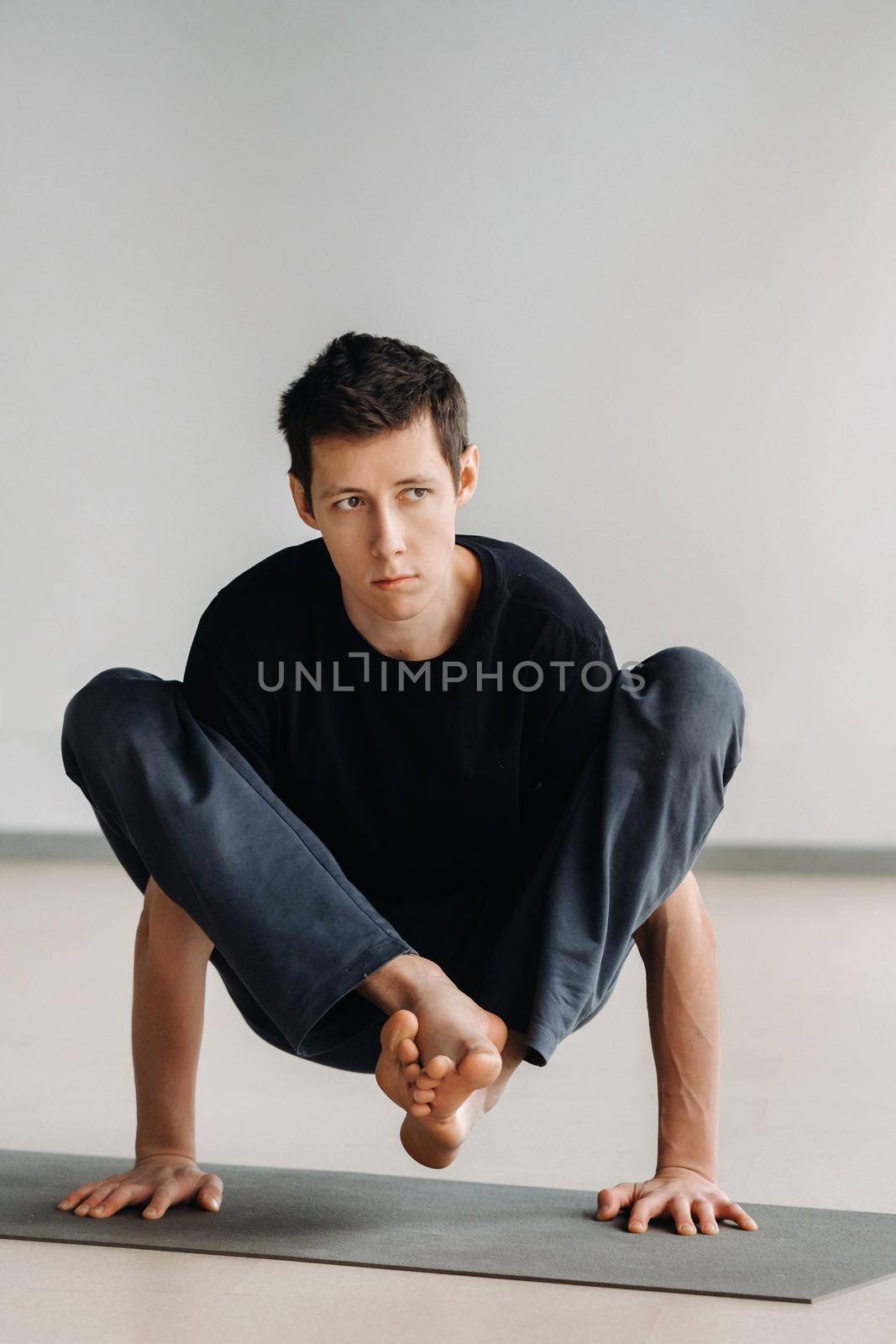 A man in a black T-shirt trains lying down doing stretches in the gym.