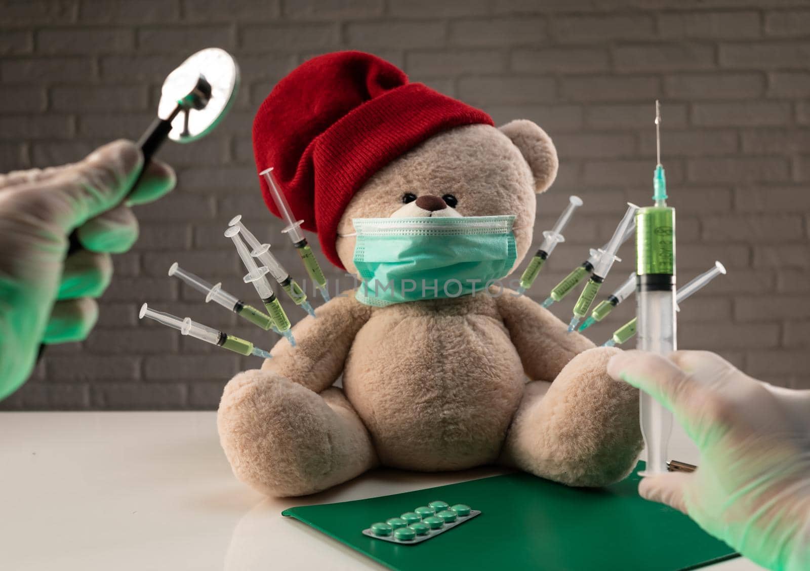 a teddy bear in a medical mask with syringes in his shoulder on the doctor's table is given a second vaccination injection against the corona virus by Rotozey