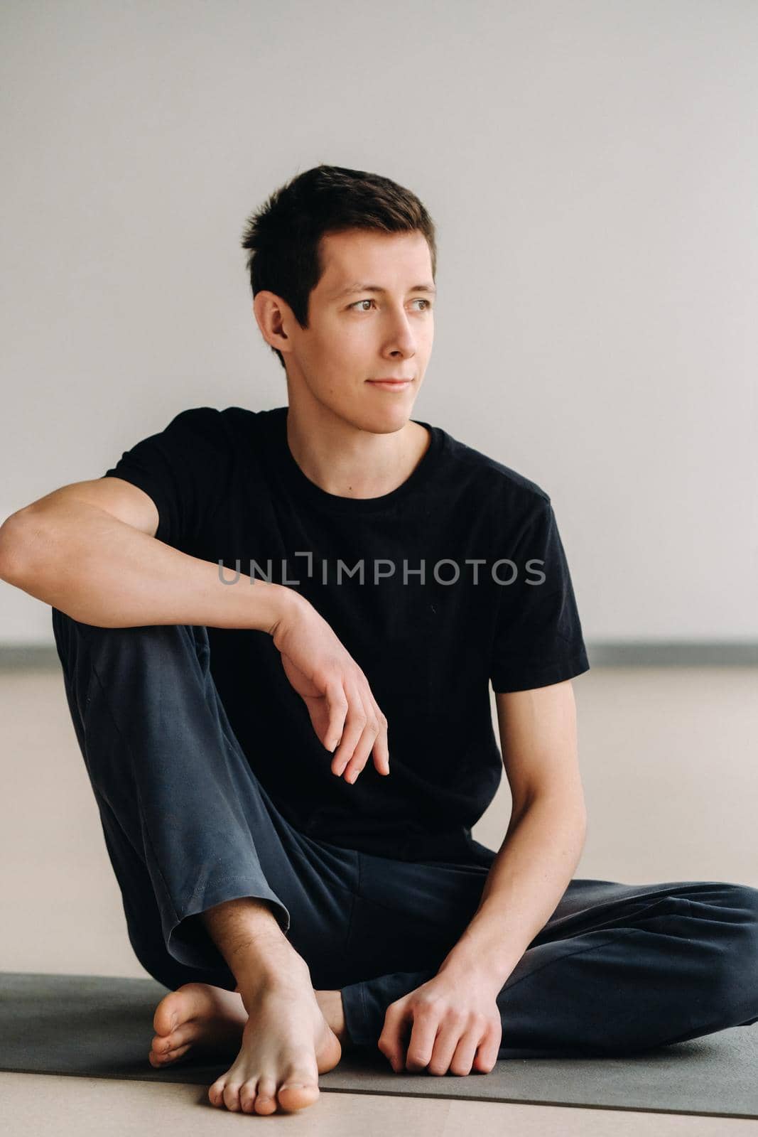 A male athlete in a black T-shirt is sitting in the gym before training and resting.