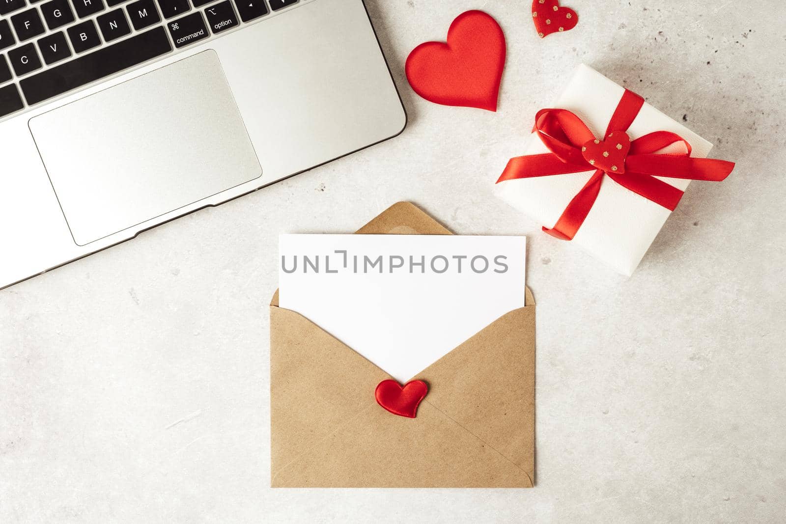 Red paper envelope with blank paper white note mockup. Flat lay of gray working table background with Valentine gift, letter, heart shape, laptop and decoration. Top view, mock up greeting card