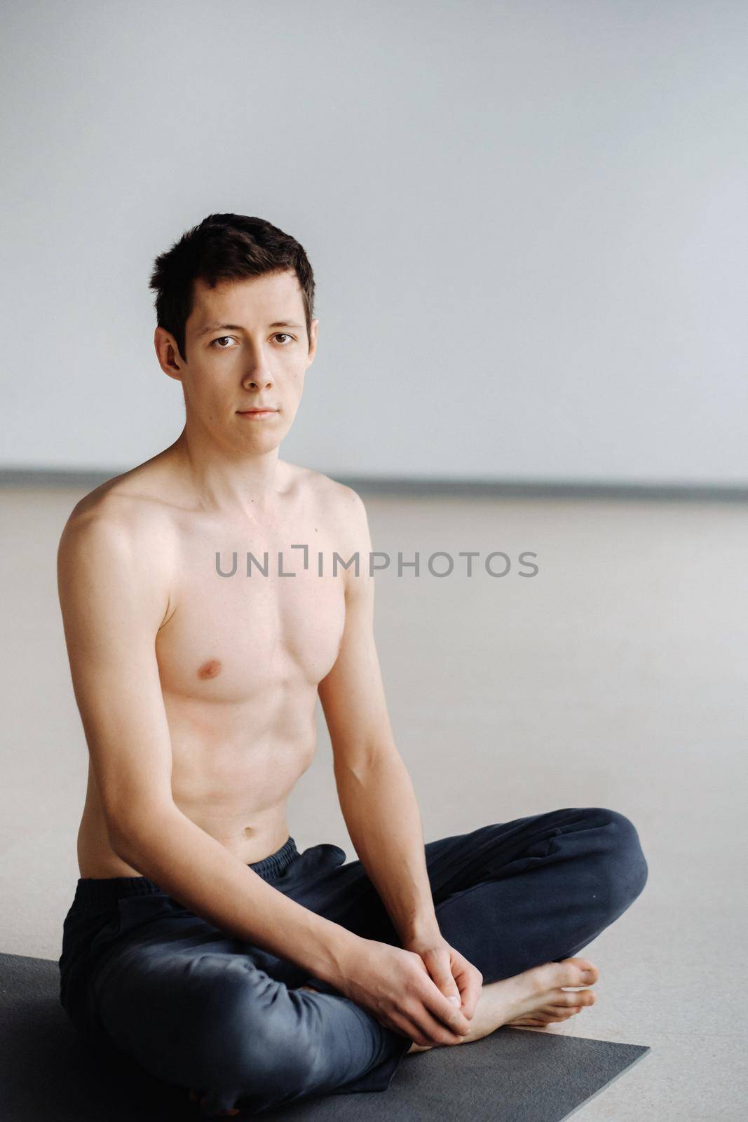 A male athlete with a bare torso is sitting in the gym before training and resting.