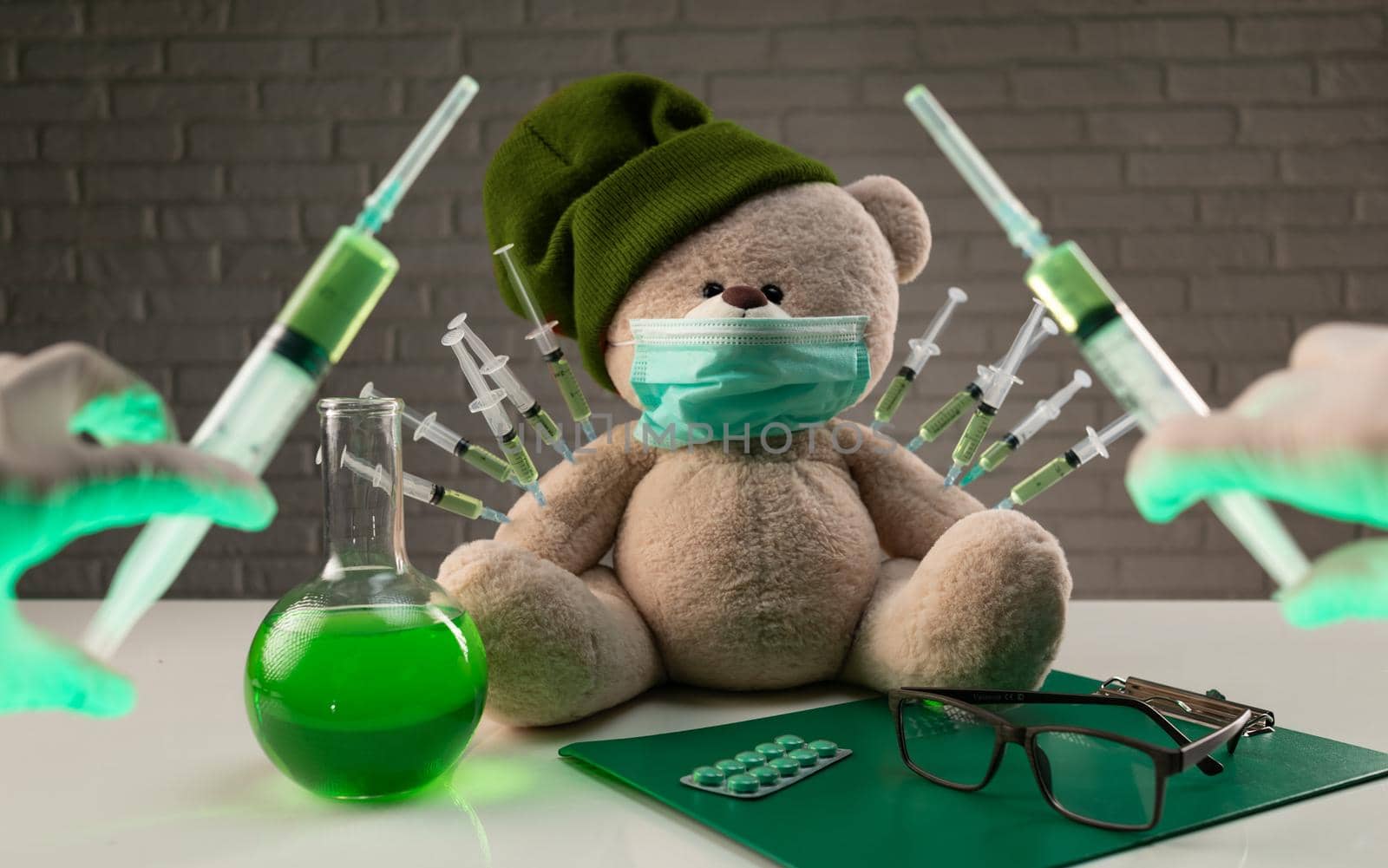 teddy bear in a medical mask with syringes in his shoulder on the doctor's table is given a second vaccination injection against the corona virus