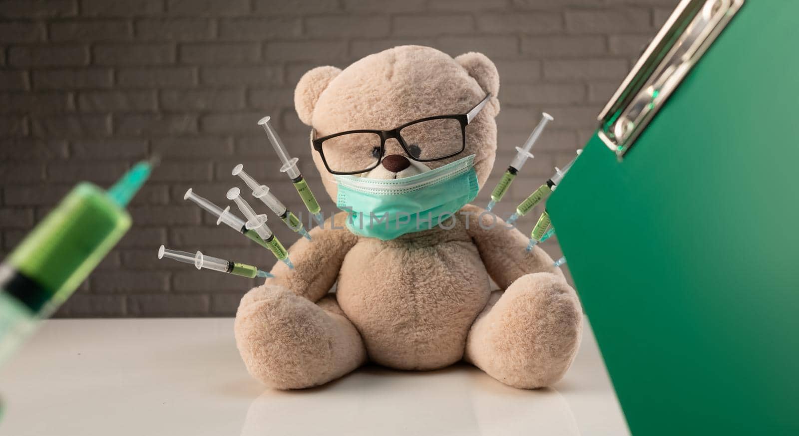 a teddy bear in a medical mask with syringes in his shoulder on the doctor's table is given a second vaccination injection against the corona virus by Rotozey