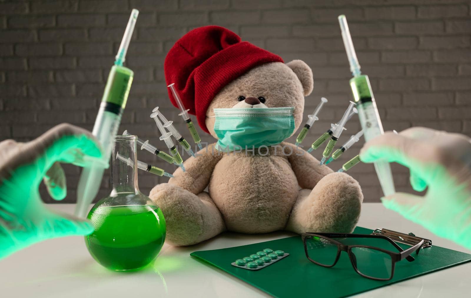 teddy bear in a medical mask with syringes in his shoulder on the doctor's table is given a second vaccination injection against the corona virus
