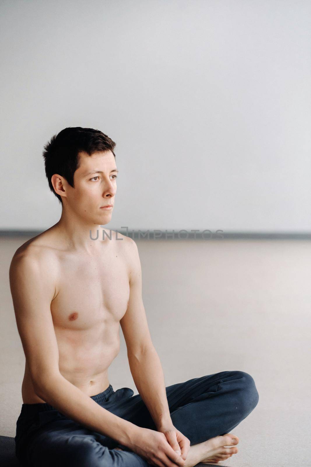 A male athlete with a bare torso is sitting in the gym before training and resting.