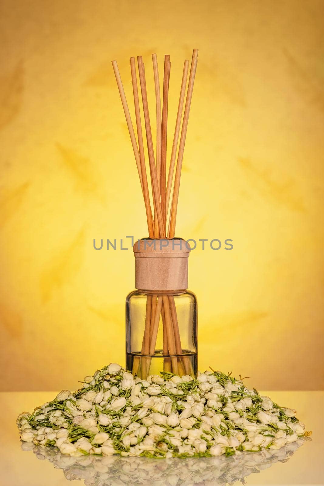 Home fragrance diffuser with wooden sticks with dried jasmine flowers on yellow background.