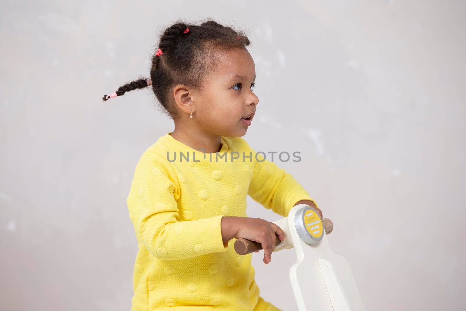 Little African American girl in a yellow dress with curly braids on a light background.