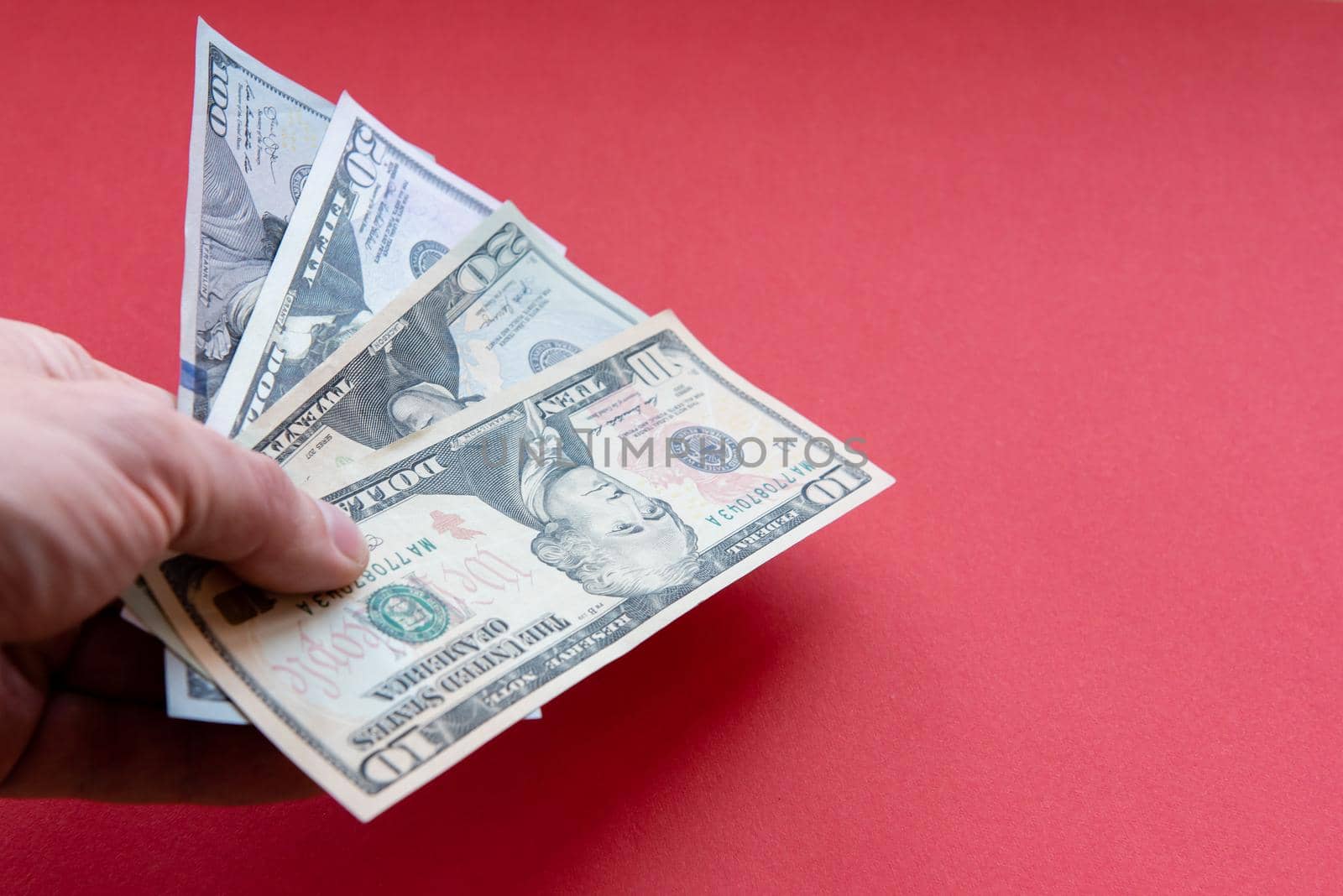 Mans hand hold dollar banknotes of different denominations Close up on red background.