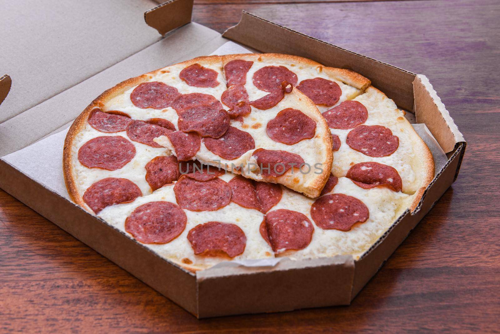Pepperoni Pizza in open carton box on wooden table, closeup.