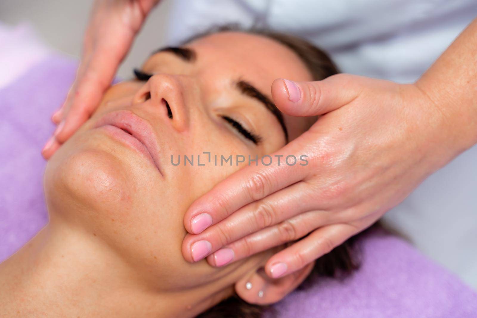 Relaxing massage. European woman getting facial massage in spa salon, side view by Matiunina