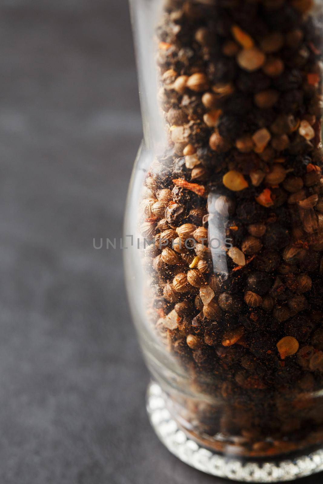 A mixture of seasonings, spices and herbs in a glass mill on a black background. Free space top view, minimalism