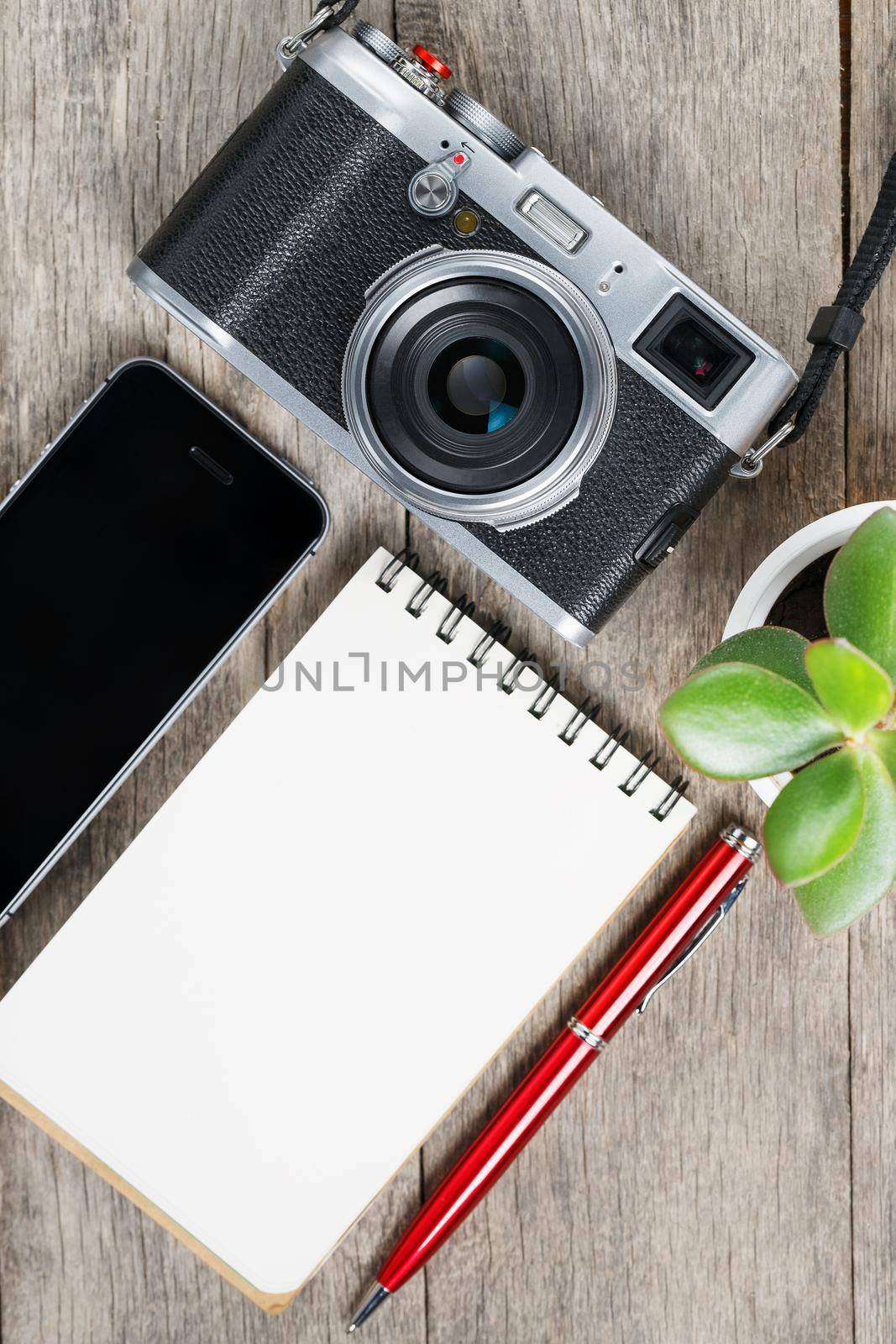Classic camera with blank notepad page and red pen on gray wooden, vintage table with telephone and green flower. The concept of the list for the photographer in travels. Country style.