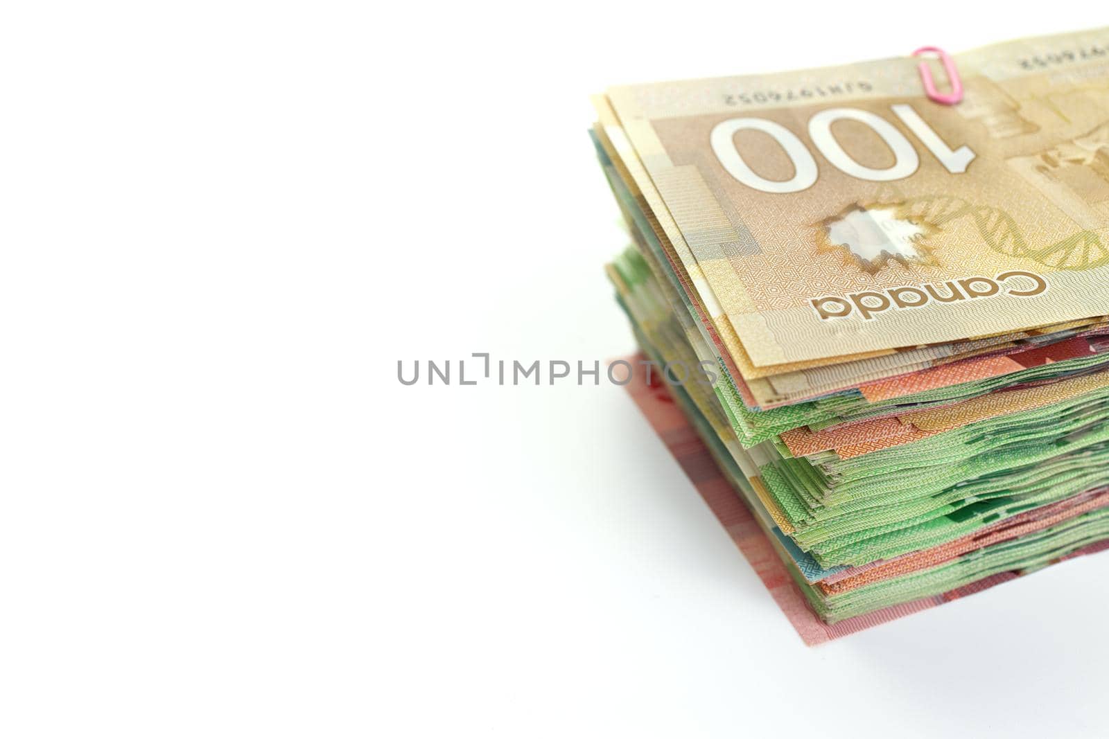 High Angle View of Large Stack of Canadian Banknotes on a White Background. Top bill is 100 one hundred and the bills below have values of 5 five, 10, ten, 20 twenty, and 50 fifty dollars. Copy Space on Left. High quality photo