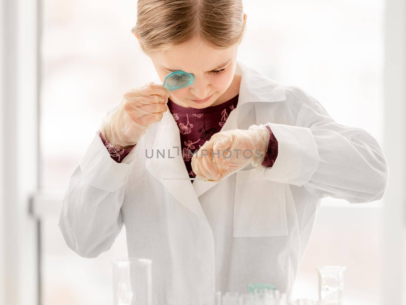 Smart girl during scientific chemistry experiment looking at glass with tests. Schoolgirl with chemical equipment on school lesson