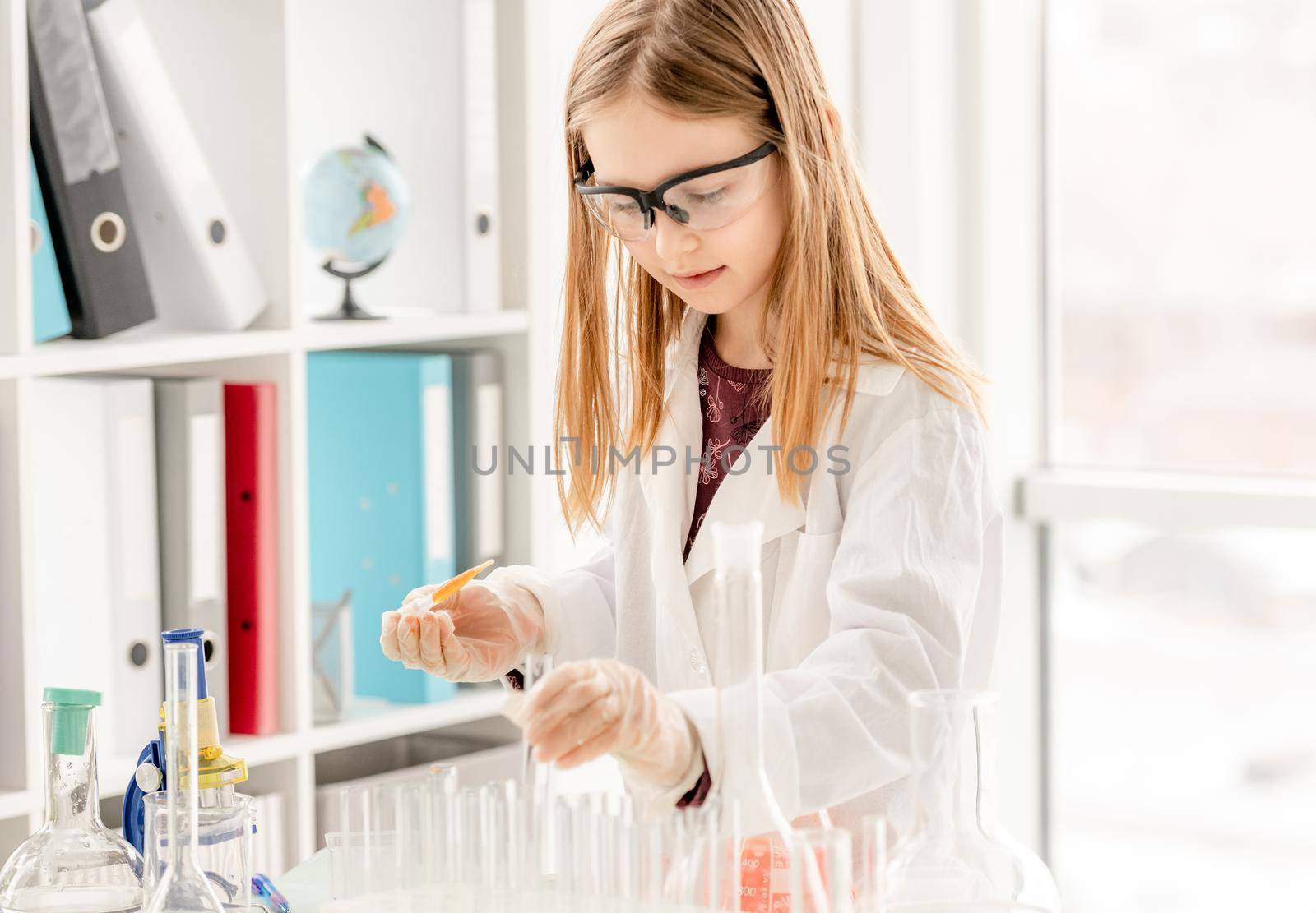 Girl doing scientific chemistry experiment wearing protection glasses and measuring liquid. Schoolgirl with test equipment on school lesson