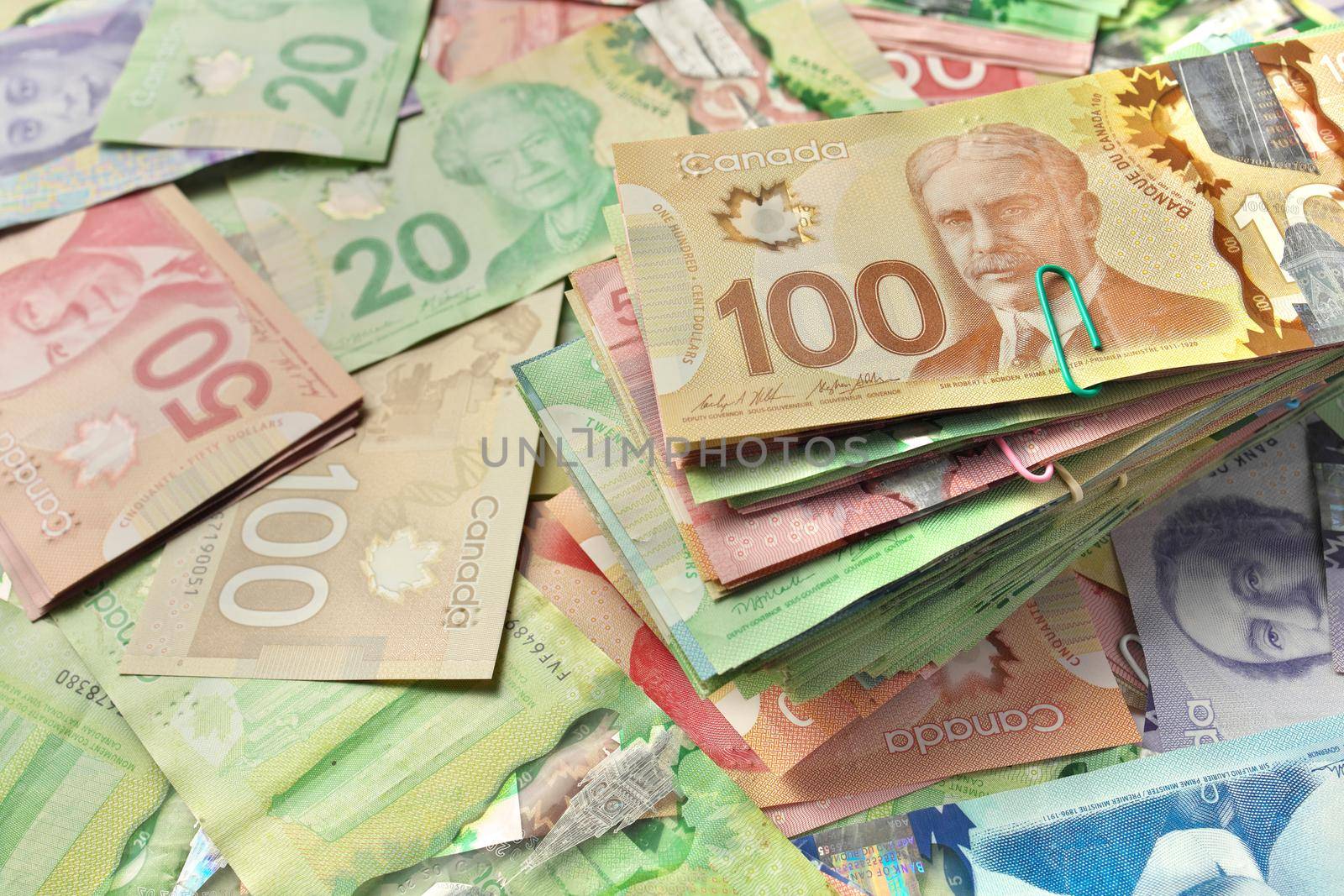 A High Angle View of Canadian Banknotes of Different Values with a Large Stack of Bills on Top. Banknotes are piled randomly on top of each other and have values of 5 five, 10 ten, 20 twenty, 50 fifty, and 100 one hundred dollars. High quality photo