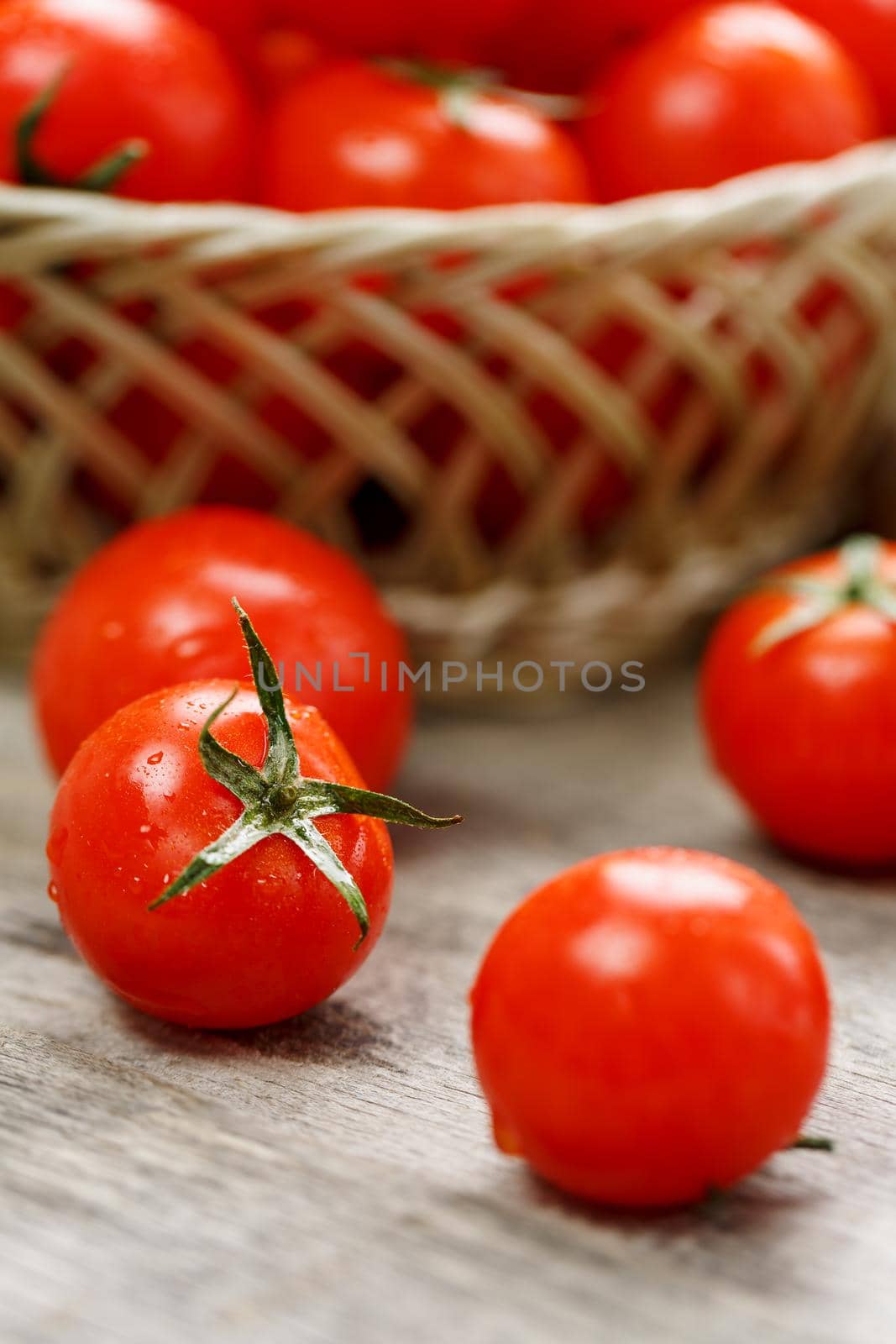 Small red tomatoes in a wicker basket on an old wooden table. Ripe and juicy cherry and burlap cloth, Terevan style country style Vertical frame