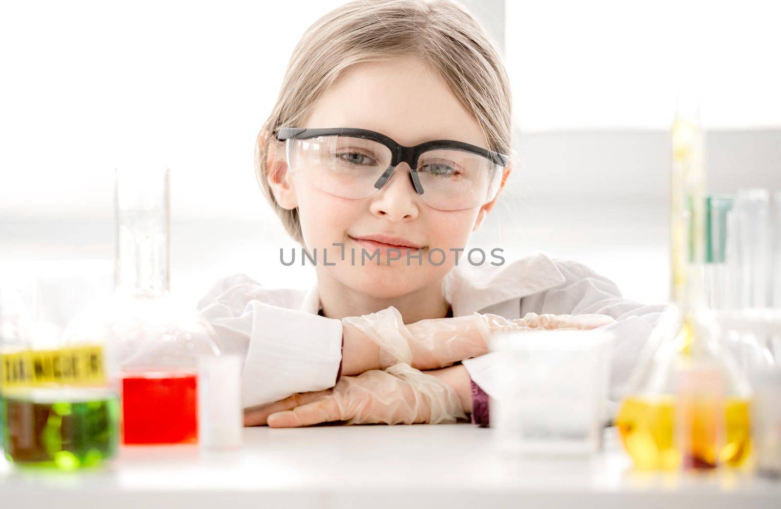 Smart girl during scientific chemistry experiment looking at camera and tubes with liquids on table. Schoolgirl with chemical equipment on school lesson portrait