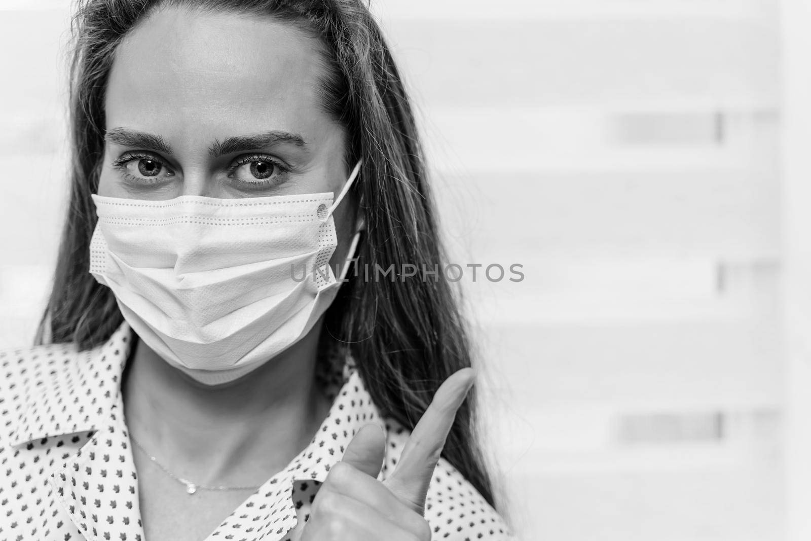 Close-up portrait of a young light brown woman in a medical mask on a light background. Finger points to the place for the inscription. Quarantine. Stay at home. Coronovirus covid-19 pandemic concept.