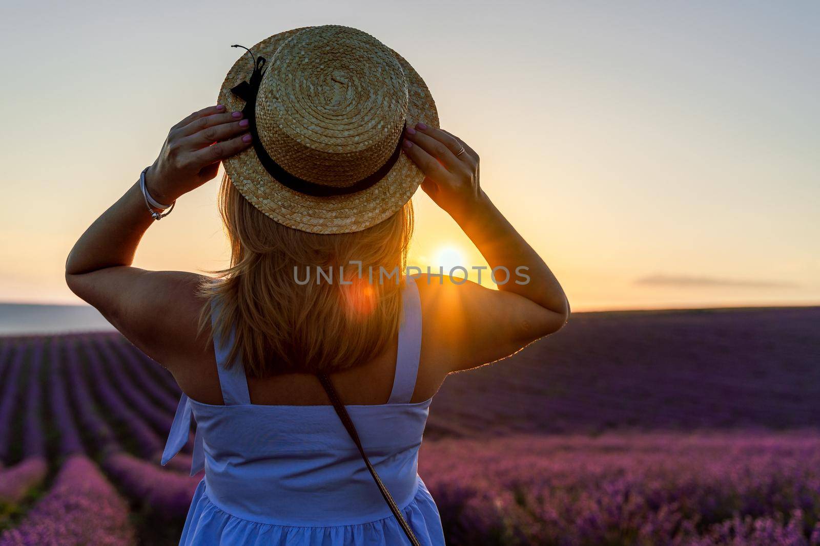 A beautiful blonde is in a lavender field. Standing all alone and holding his hat in his hands. Aromatherapy concept, lavender oil, lavender photo shoot