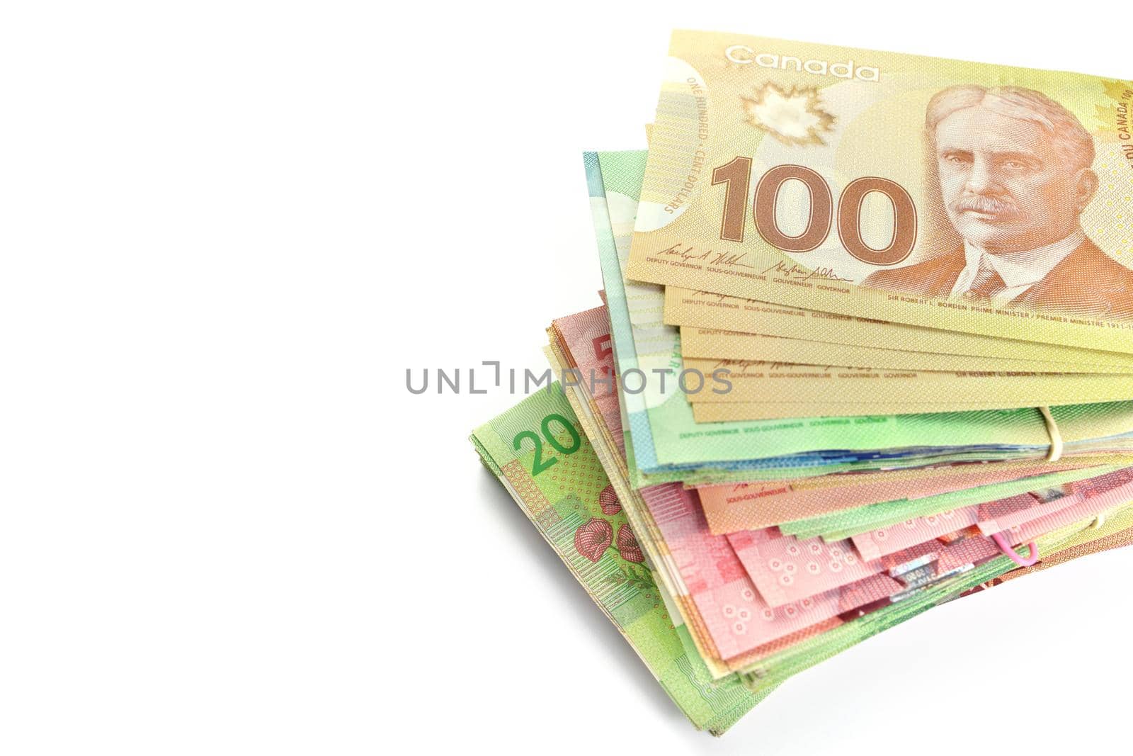 High Angle View of Large Stack of Canadian Banknotes on a White Background. Stack is slightly fanned. Top bill is 100 one hundred and the bills below have values of 5 five, 10 ten, 20 twenty, and 50 fifty dollars. Copy Space on Left. High quality photo