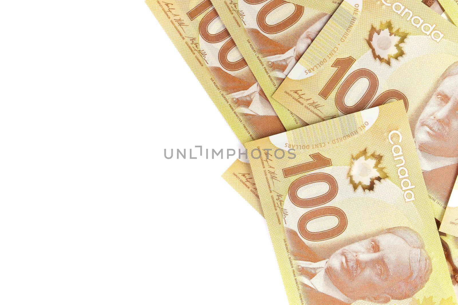 A Directly Above Image of Crisp Canadian 100 One Hundred Dollar Bills on a White Background. Banknotes are piled randomly on top of each other. Plenty of White Copy Space on Frame Left. High quality photo