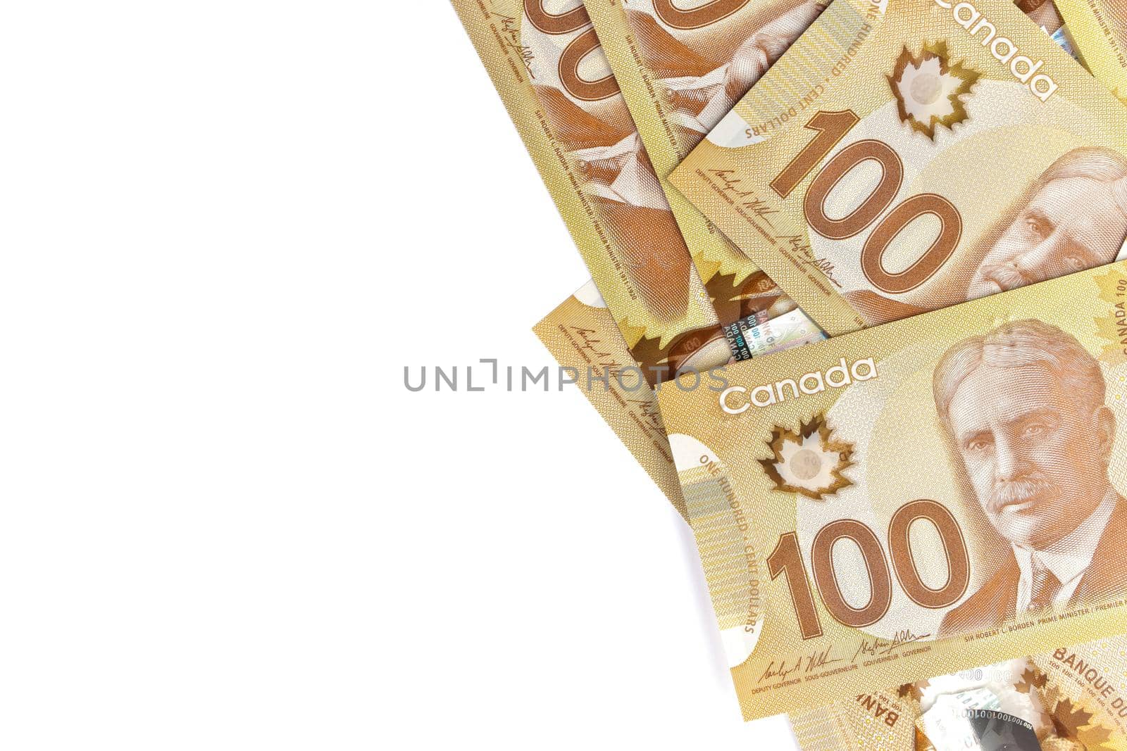 A Directly Above Image of Crisp Canadian 100 One Hundred Dollar Bills on a White Background. Banknotes are piled randomly on top of each other. Plenty of White Copy Space on Frame Left. High quality photo