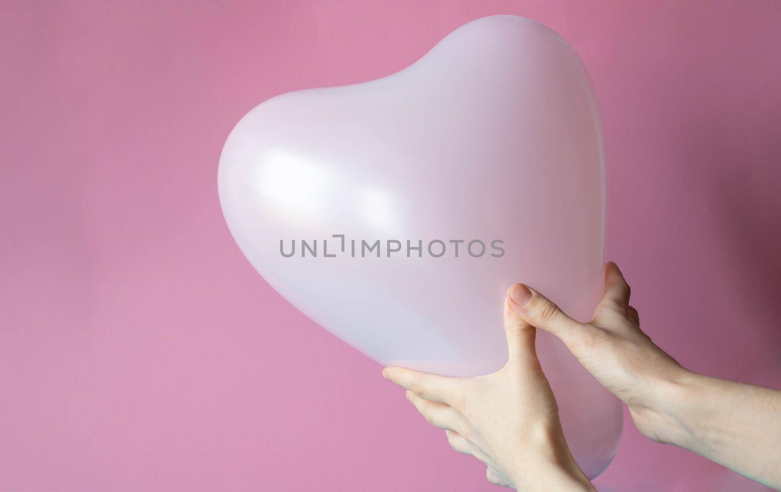Women's hands hold a pink ball in the shape of a heart, highlighted on a pink background. by lapushka62