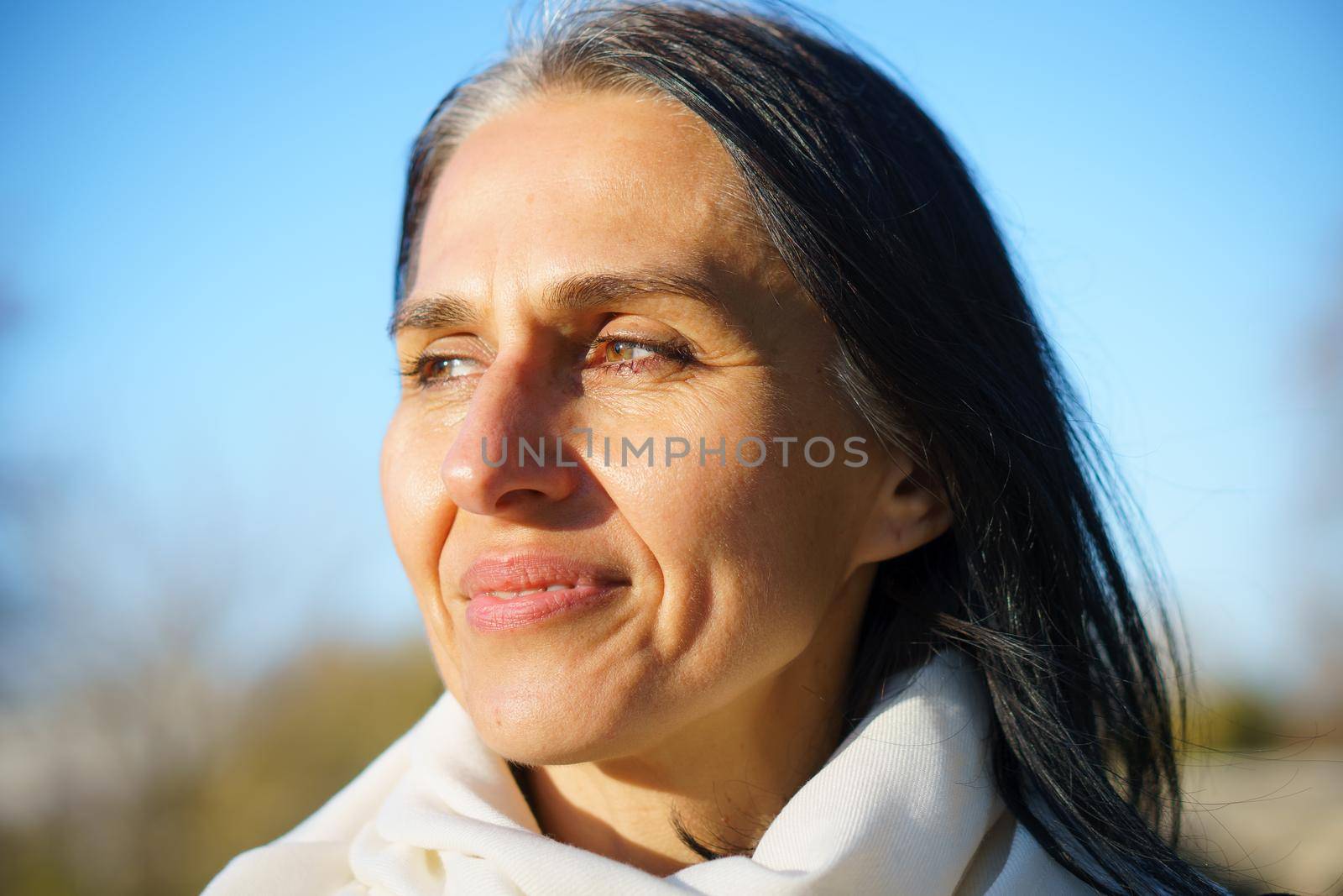 Profile side view portrait of attractive cheerful dreamy grey-haired middle-aged woman relaxing outdoors during sunny day.