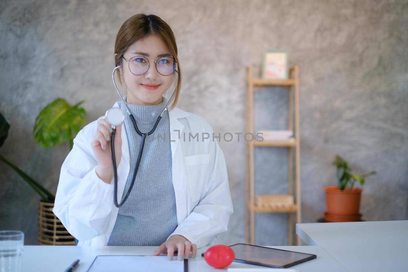 Portrait of doctor smiling wearing eyeglasses and showing stethoscope tools at office in private clinic. Medicine and health care and insurance concept. by itchaznong