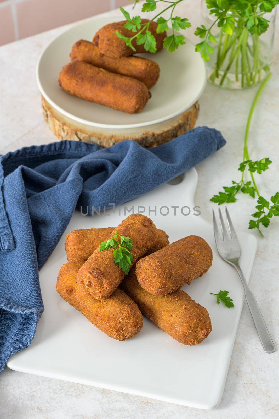 Meat croquets and parsley leaves on white ceramic dishes in a kitchen counter top.