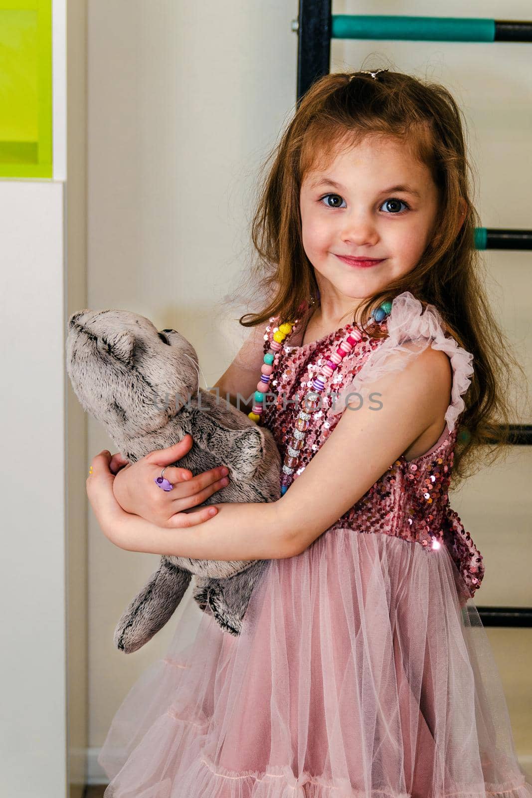 A little girl in a pink dress with a plush toy plays in her room, close-up.