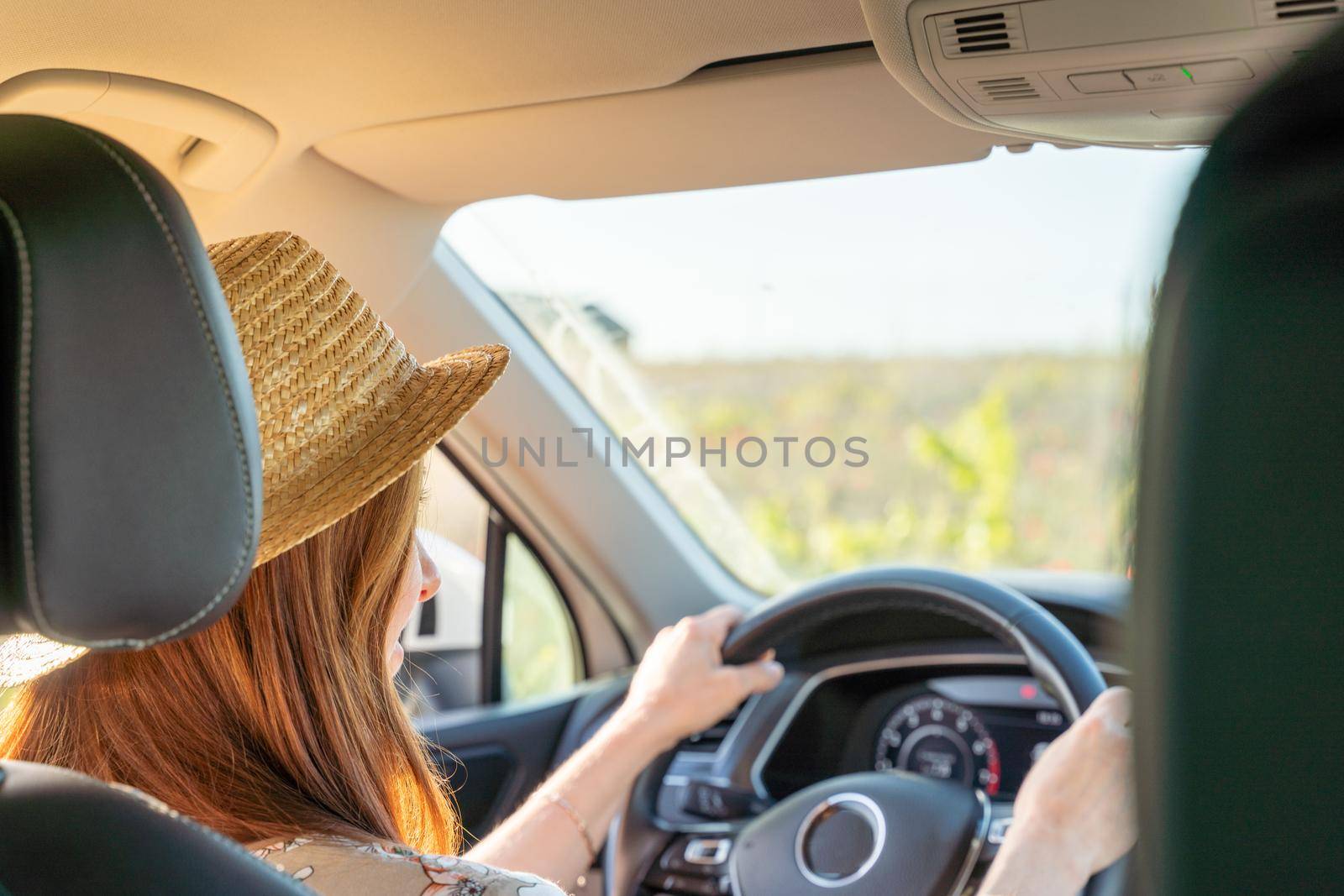 A woman in a hat and a colored dress is sitting at the wheel of a car, the view from behind, the window shows the field. by Matiunina