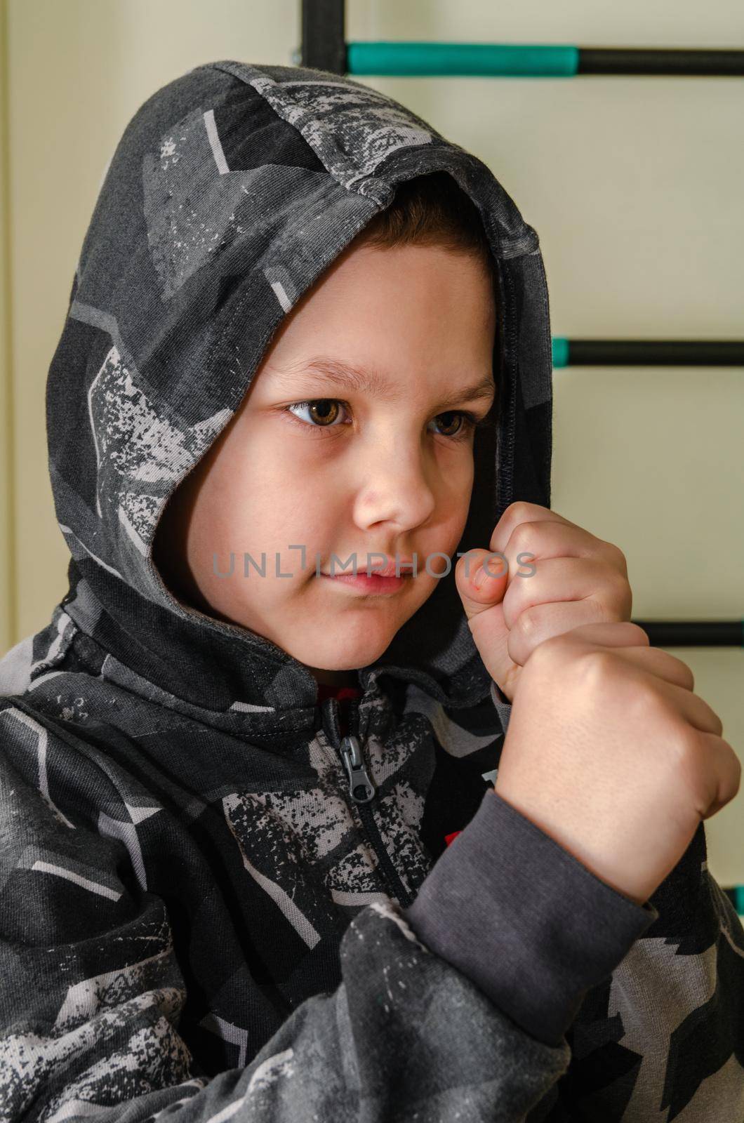 A little boy stands in a fighting stance in a hood. by Sergey