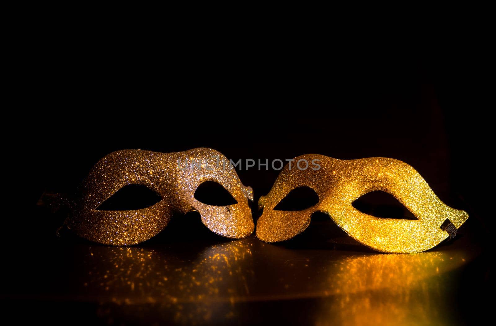 two shiny gold and silver carnival masks on black background