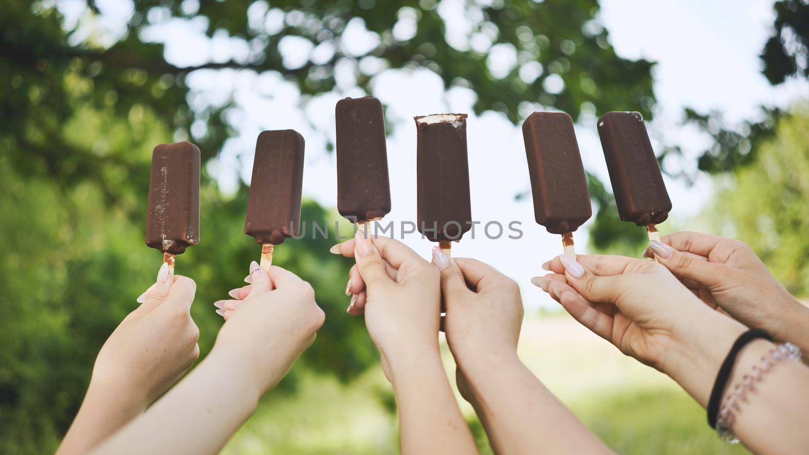 Friends hold chocolate ice cream on a stick in a row. by DovidPro