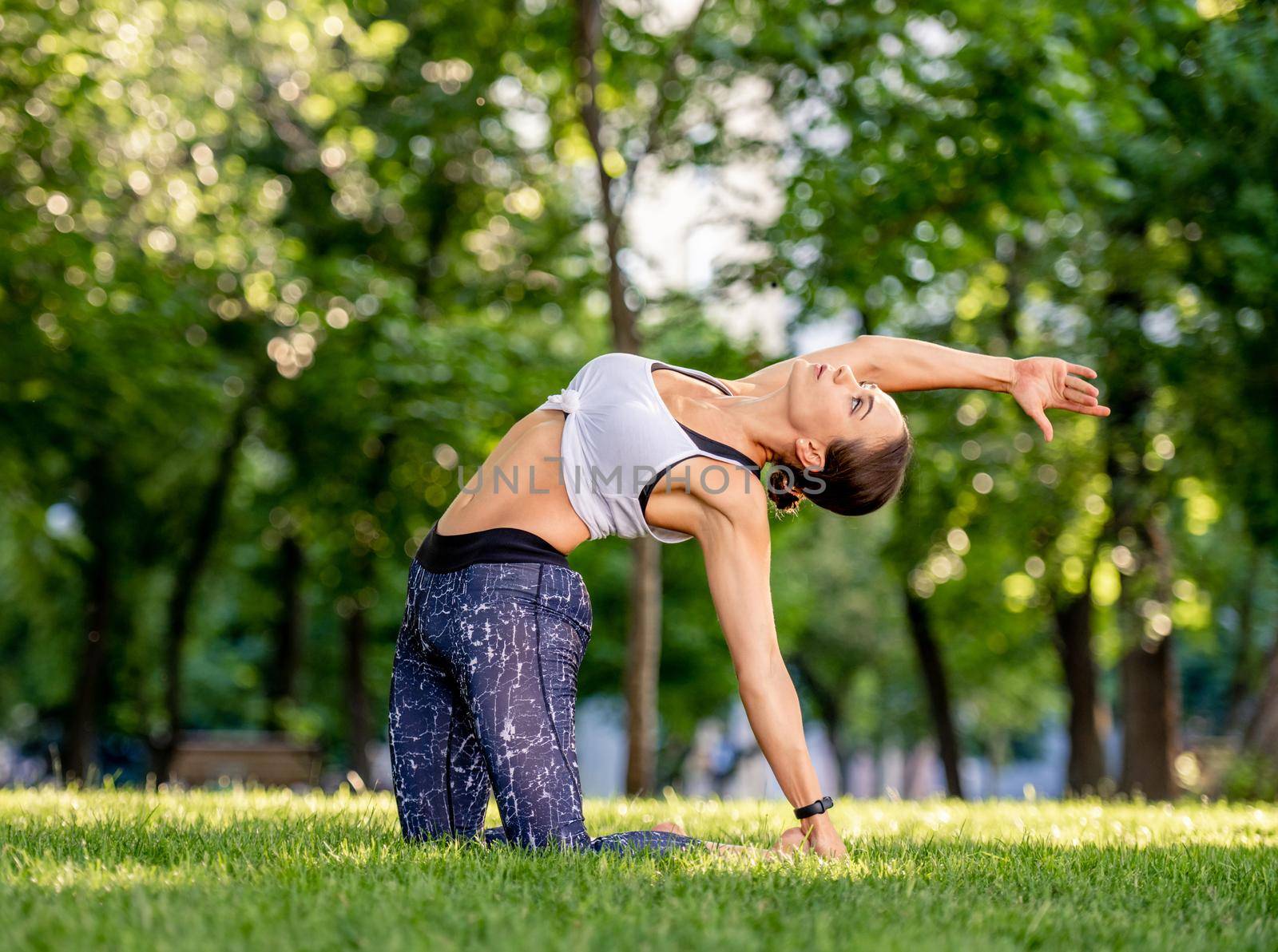 Sport girl doing yoga at nature and training her balance. Young woman exercising and stertching her body in summertime