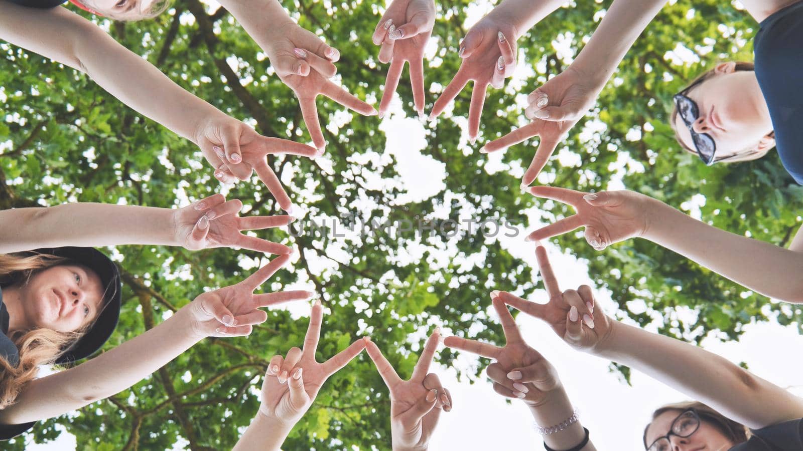 Girlfriends join fingers in a circle against the background of tree branches