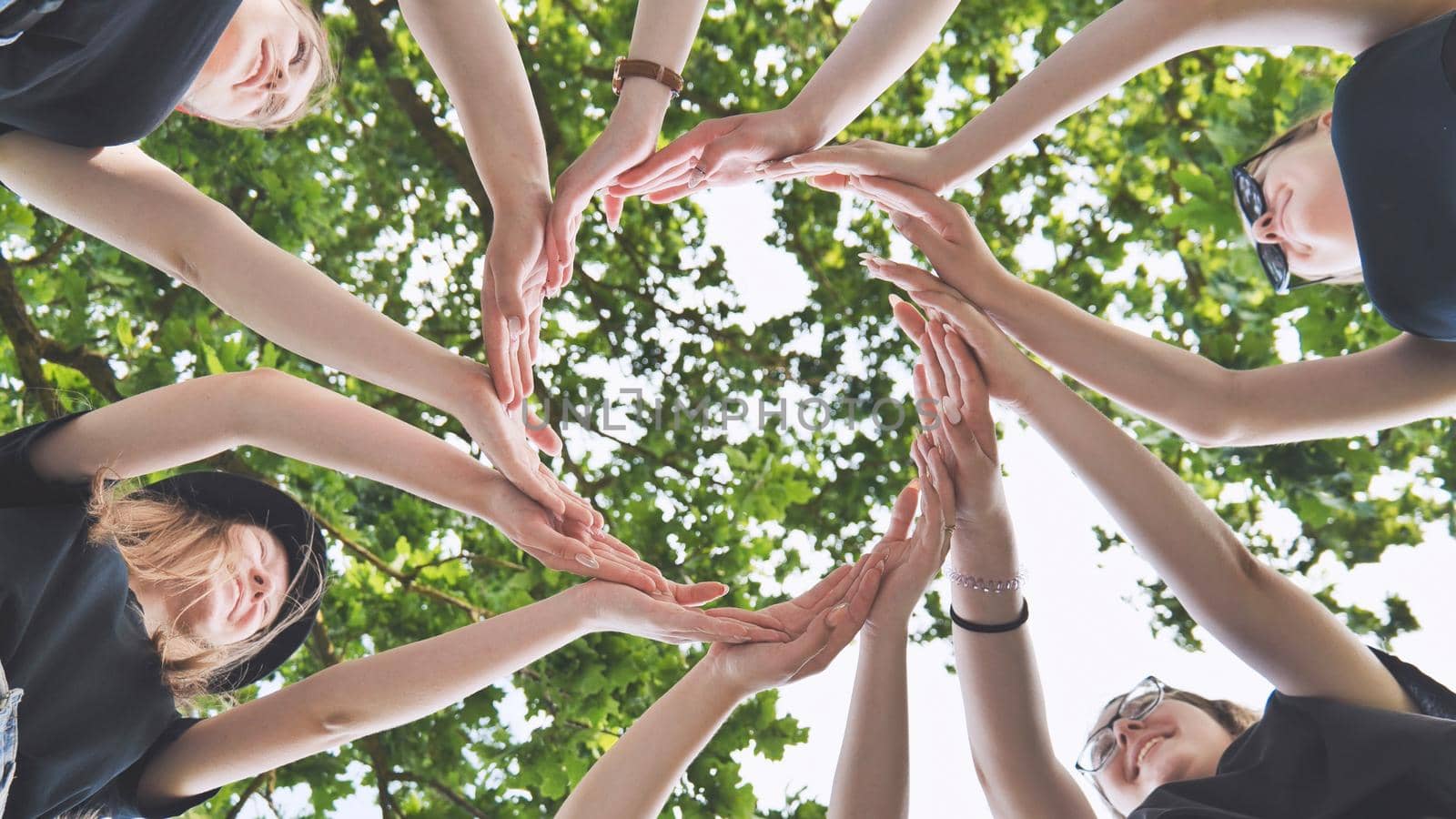 The girlfriends join their palms in a circle against the background of tree branches