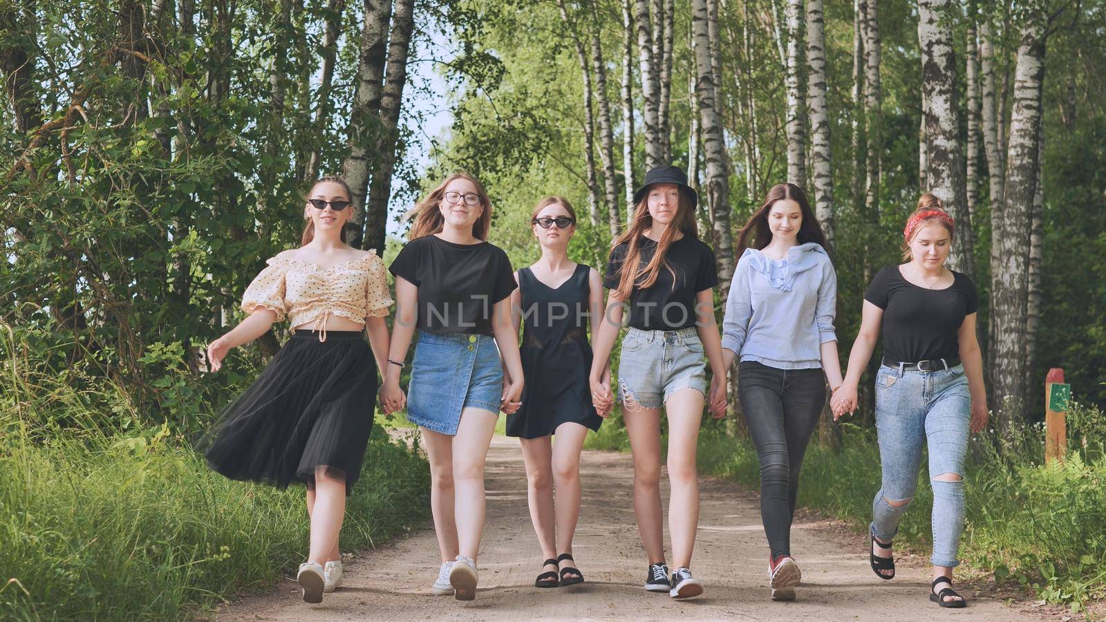 Schoolgirl friends are walking outside the city along a forest road. by DovidPro