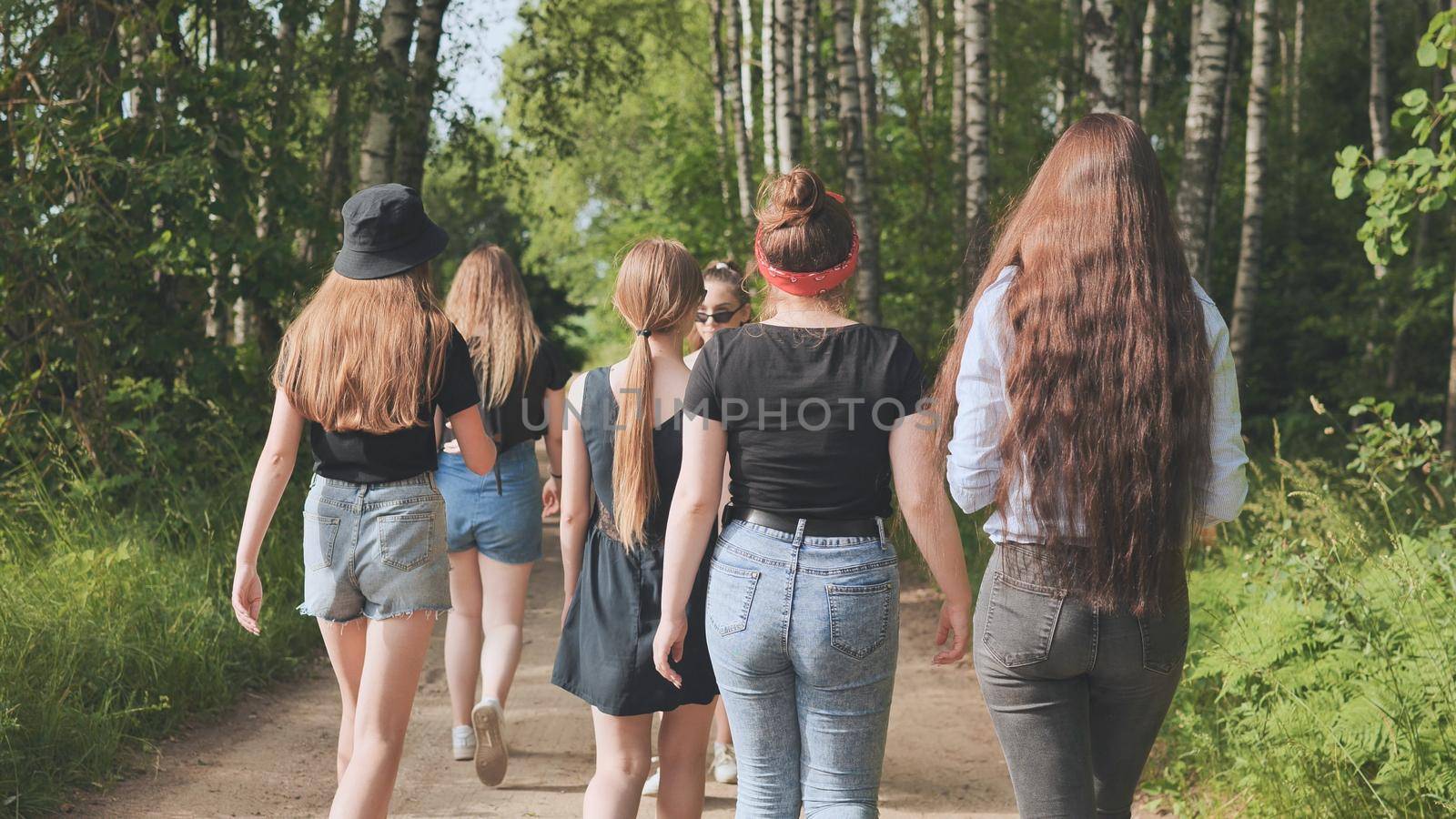 Schoolgirl friends are walking outside the city along a forest road. by DovidPro