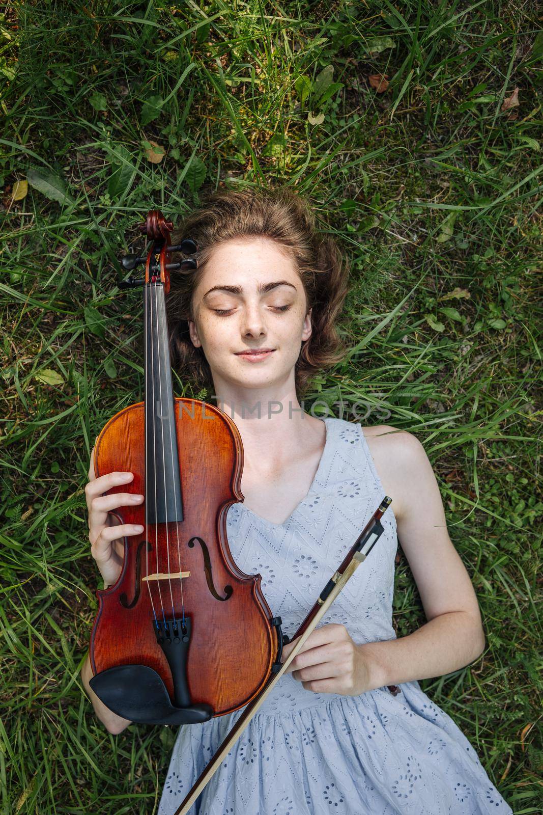 The girl lies with a violin on the grass in a city park