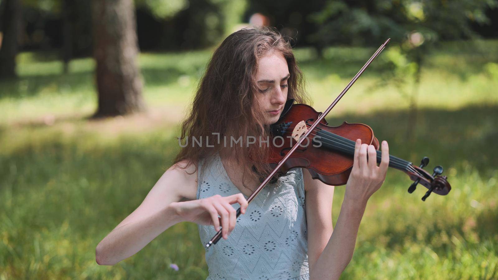A young girl plays the violin in the city park. by DovidPro