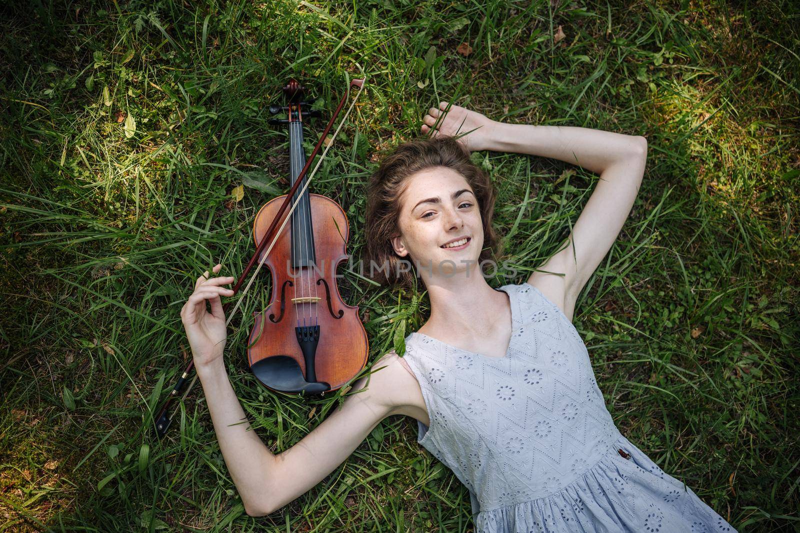 The girl lies with a violin on the grass in a city park