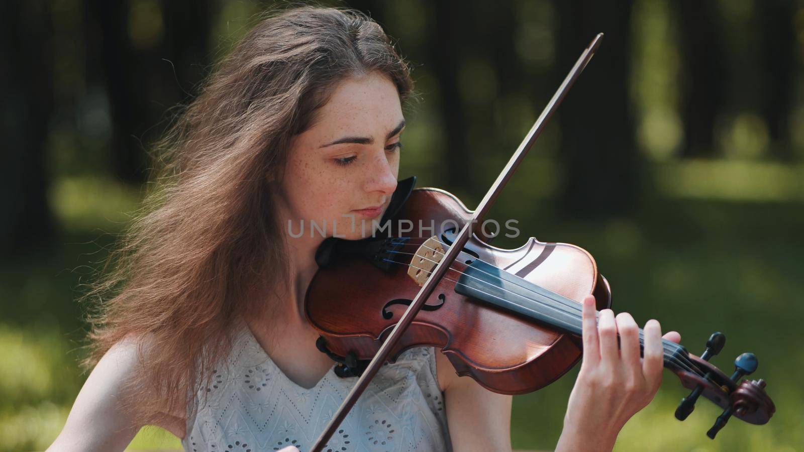 A young girl plays the violin in the city park