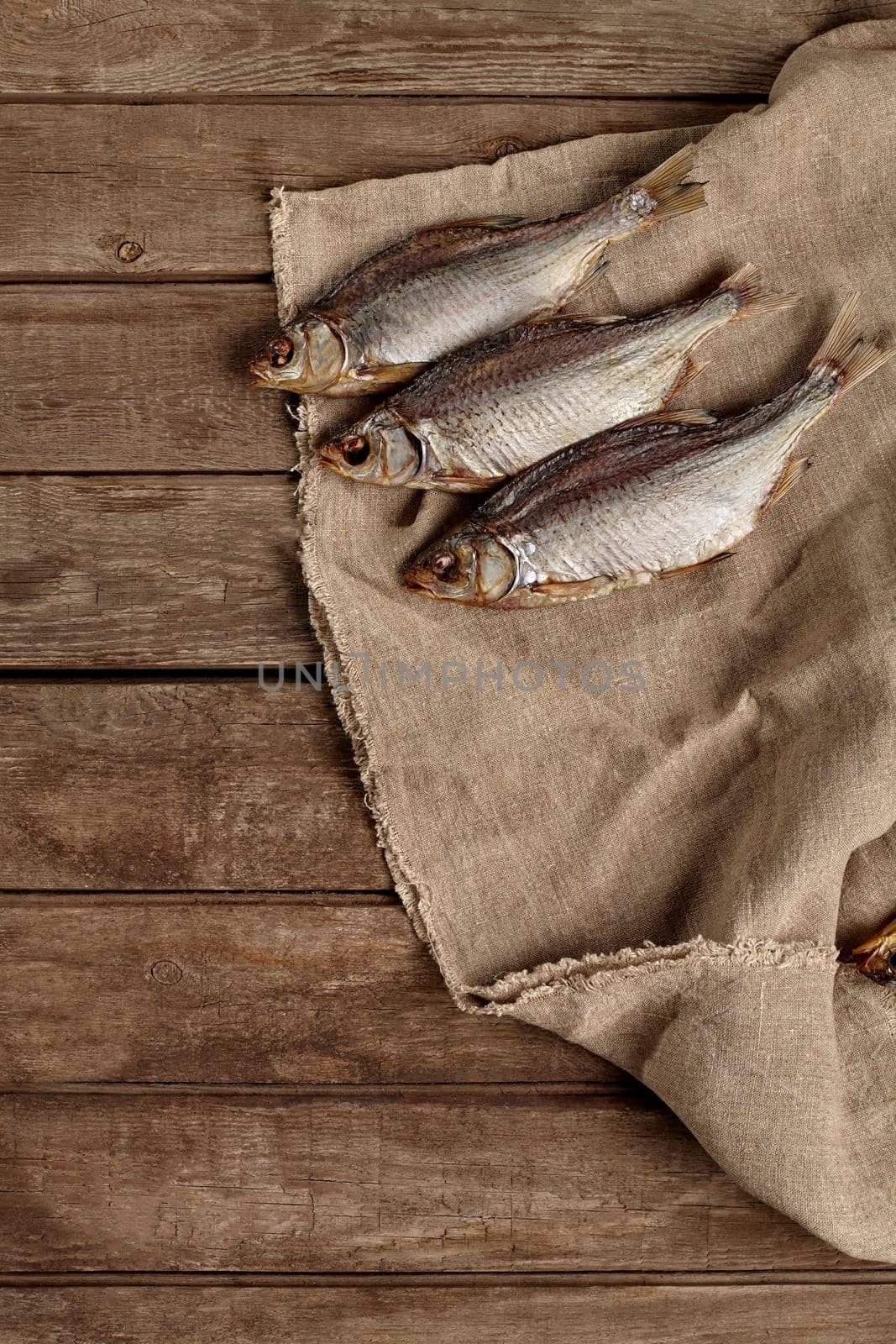 Three salted air-dried roach lying on sackcloth on background of rough rustic wooden planks, top view with copyspace