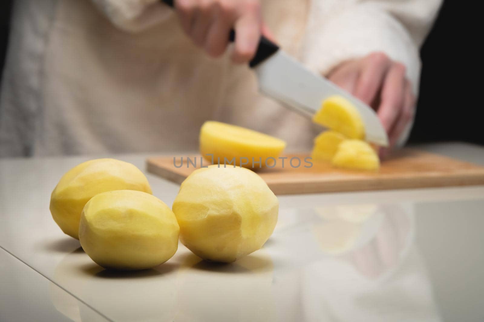 Close-up of female hands cutting fresh peeled potatoes on a cutting wooden board. Vegetarian food preparation.