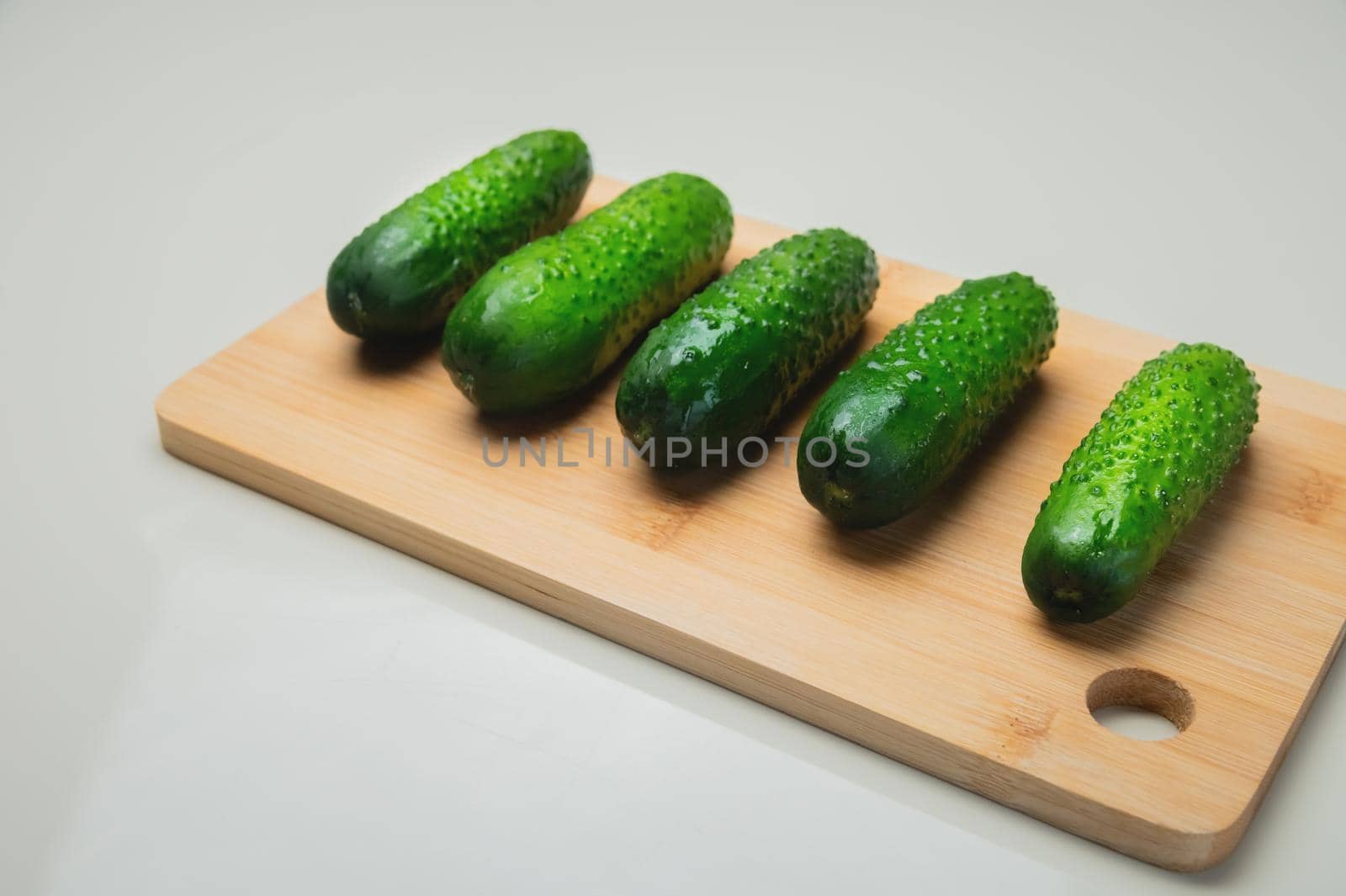 Close-up of several fresh cucumbers lie on a wooden cutting board on a white table. copy space vegetarian food.