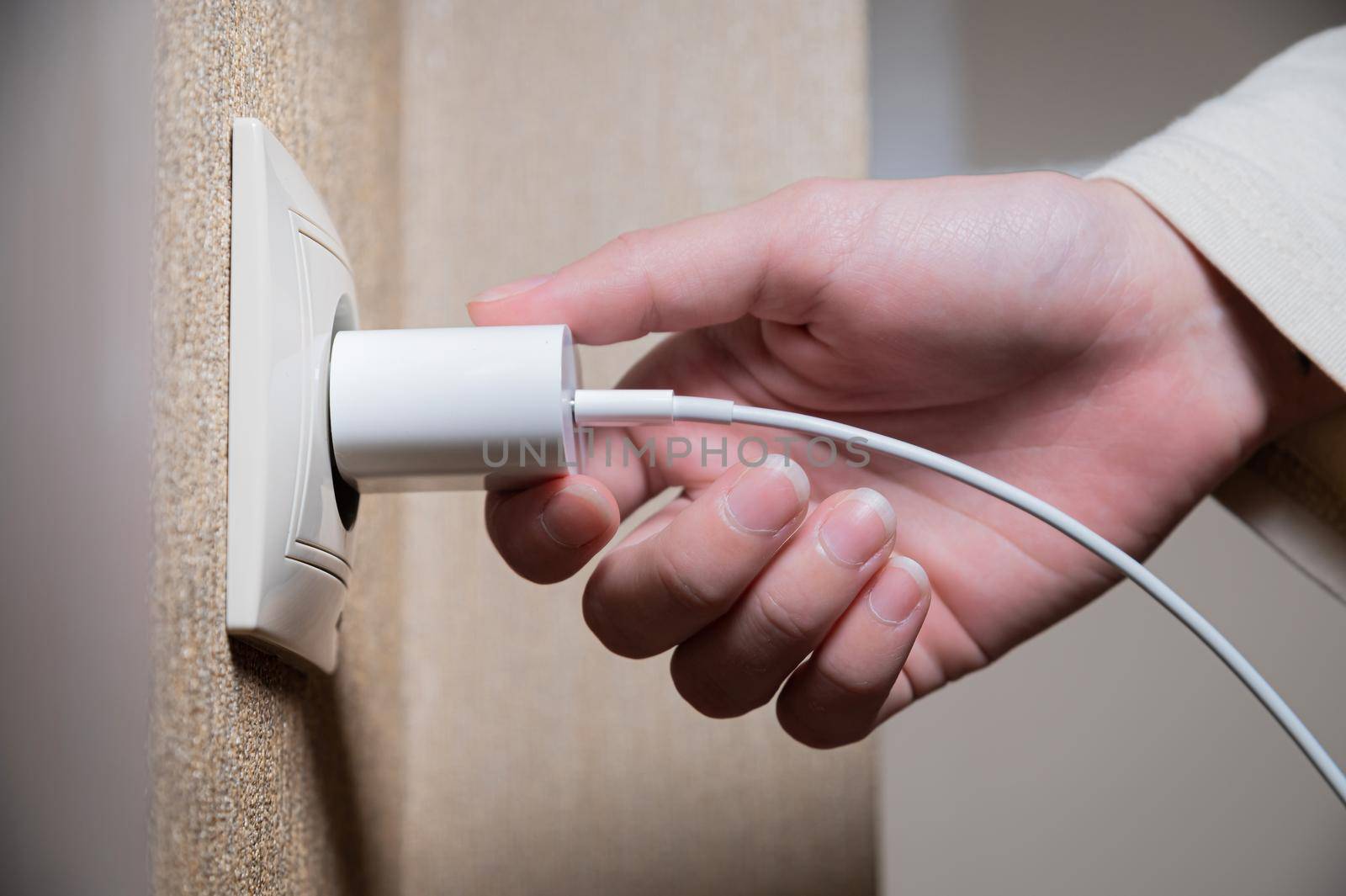 Close-up of a woman's hand inserting a white usb charger into a 220 volt socket by yanik88
