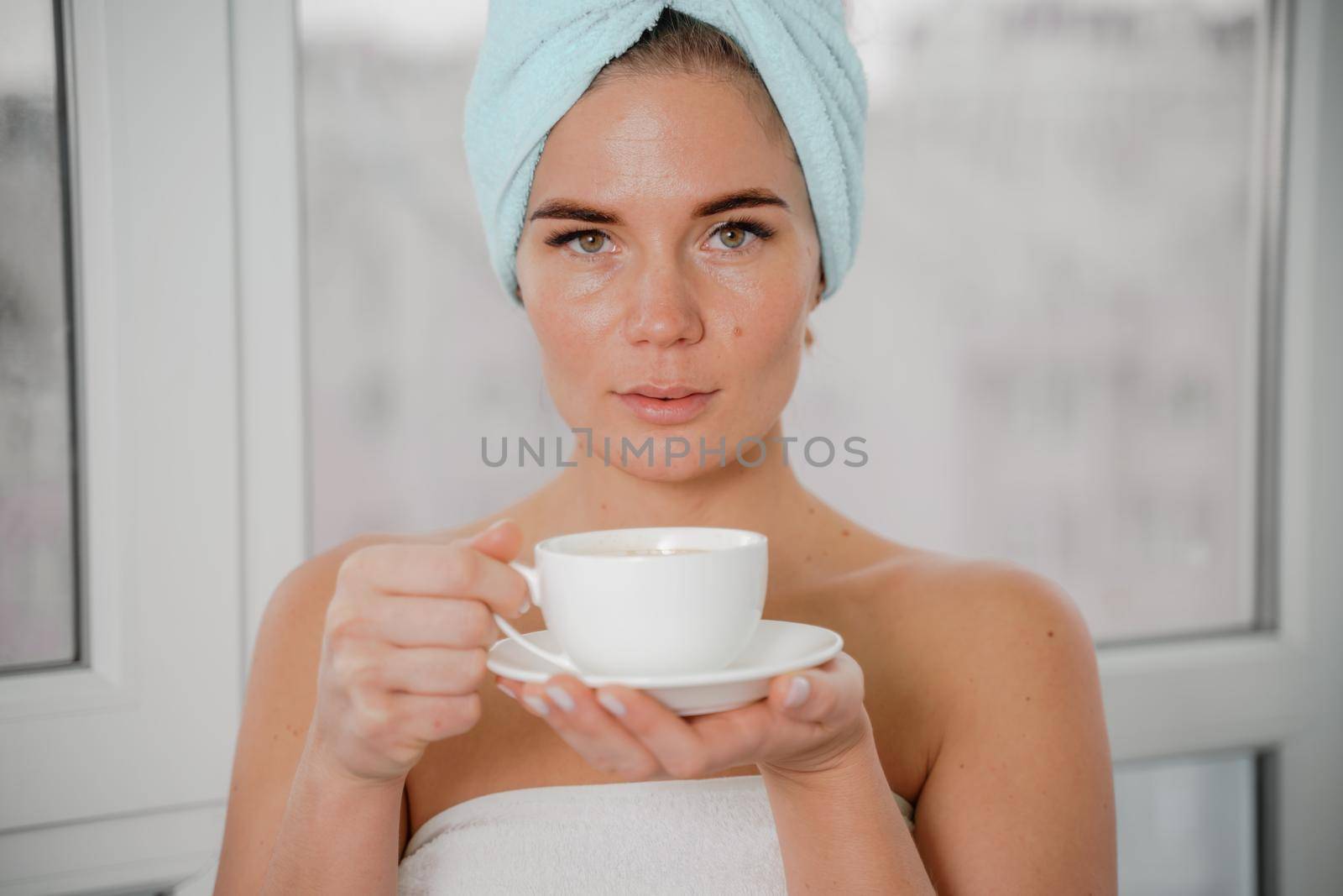 Young serene relaxed woman in spa bath towel drinking hot beverage tea coffee after taking shower bath at home. Beauty treatment, hydration concept